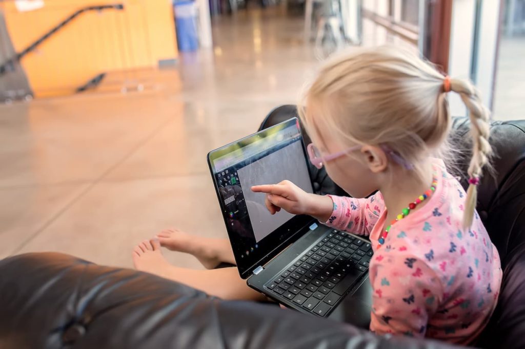 Elementary girl using Chromebook while sitting in a chair.